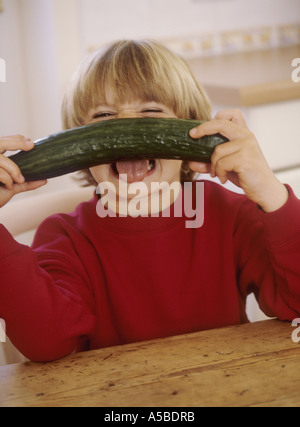 Jeune garçon assis dans une cuisine, avec un concombre - s'amusant Banque D'Images