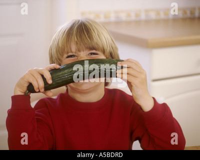 Jeune garçon assis dans une cuisine, avec un concombre - s'amusant Banque D'Images