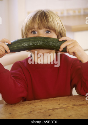 Jeune garçon assis dans une cuisine, avec un concombre - s'amusant Banque D'Images