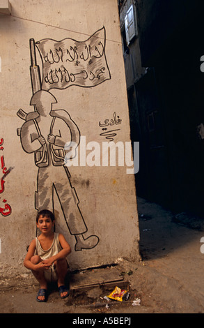 Un garçon assis contre un mur avec des graffitis au camp de réfugiés de Chatila à Beyrouth Banque D'Images