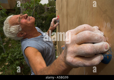 Un homme âgé d'escalade sur un mur d'escalade artificiel avec portrait climber holding grips et regarder de l'avant pour poignée suivante Banque D'Images