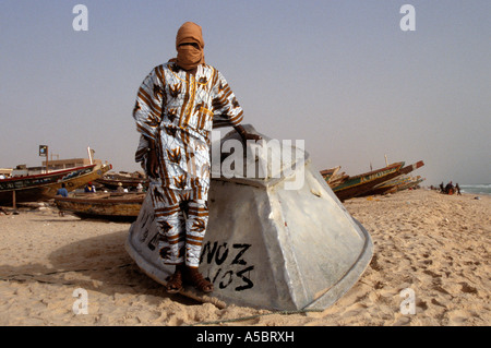 Pêcheur mauritanien en costume traditionnel appuyé contre retroussé fishing boat on beach, portrait, Nouakchott, Mauritanie, Afrique Banque D'Images