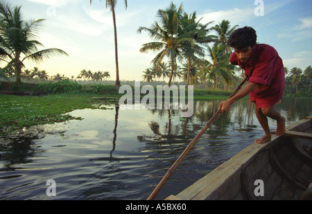 Un homme à l'aide d'une perche pour pousser son bateau dans les Backwaters du Kerala, Inde Banque D'Images