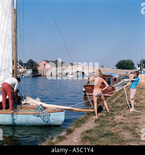 Yacht amarrage famille sur la rivière Thurne au potter Heigham, Norfolk. Woman in bikini, l'homme en pantalon, garçon en short. Banque D'Images