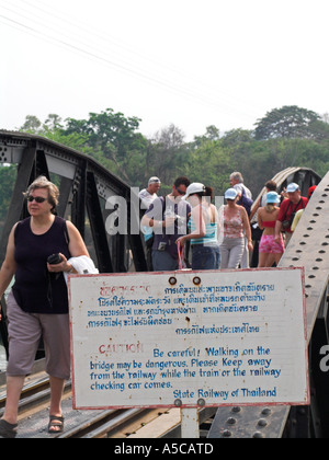 Les touristes et les visiteurs à pied passé attention mise en garde sur le pont sur la rivière Kwai Kanchanaburi Thaïlande Banque D'Images