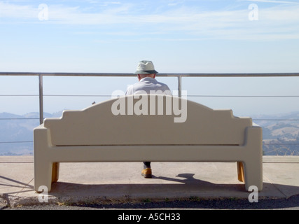 Une vue de l'arrière d'un homme âgé portant un chapeau de toile blanche, assis sur un banc blanc Banque D'Images