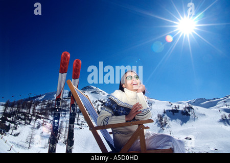 Autriche, femme assise sur une chaise longue dans la neige des Alpes, smiling, low angle view Banque D'Images