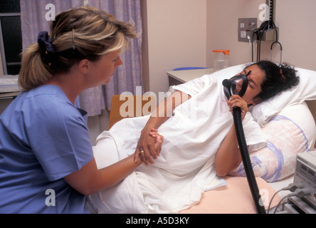 sage-femme soutenant une femme hispanique en travail à l'hôpital avec un masque à gaz et à air Banque D'Images