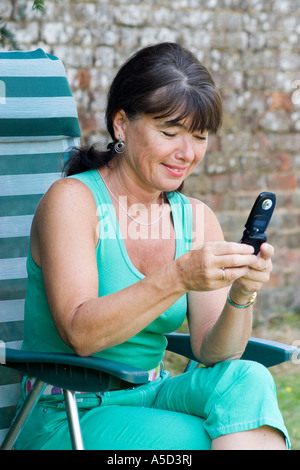 Femme d'âge moyen dans la région de garden assis à l'aide de mobile phone smiling Banque D'Images