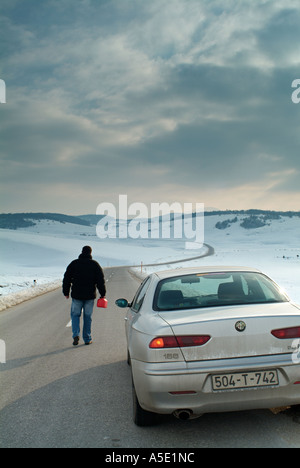 L'homme commence la longue marche le long d'une route de campagne isolée en hiver pour trouver du carburant pour sa voiture en panne Banque D'Images