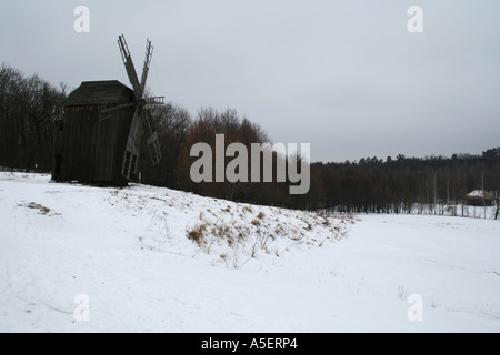 Moulin à vent en bois solitaire dans un champ ukrainien enneigé sous un ciel nuageux. Banque D'Images