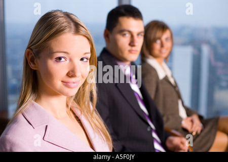 Groupe de personnes regardant la caméra se concentrer sur le visage de la première personne s'il n'y Grande fenêtre avec vue sur la grande ville derrière eux Banque D'Images