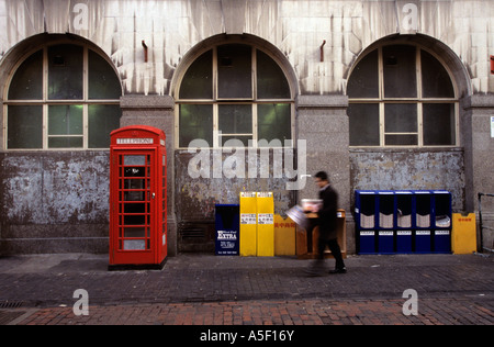 Un homme qui marche le long d'un trottoir avec une cabine téléphonique rouge classique sur la gauche Banque D'Images