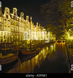 Vue de nuit panoramique de la rangée de maisons typiquement hollandais avec des fenêtres lumineuses aux côtés de canal à Amsterdam Pays-Bas Banque D'Images