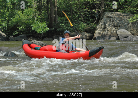 Jeune garçon dans les pagaies de kayak gonflable sur une section d'eau vive de la rivière. Banque D'Images