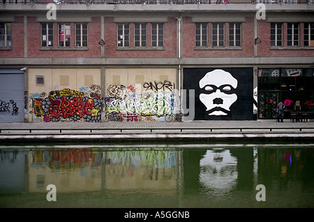 Peintures murales et graffiti ornent le mur d'un bâtiment industriel sur le Canal Saint Martin une voie d'eau dans la ville de Paris Banque D'Images