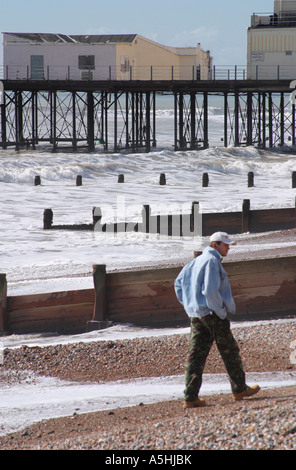 Homme marchant à shingle près de Littlehampton Pier à marée haute. Banque D'Images