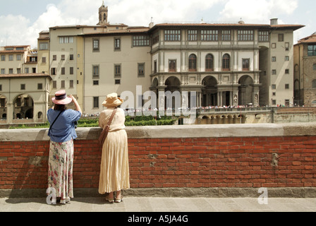 Florence deux femmes se placer à côté de l'Arno à admirer la Galerie des Offices sur la rive nord de chaleur de l'été jour Banque D'Images