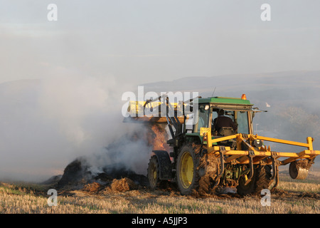 Tracteur jaune et brûlant dans le champ de chaume, East Lothian, UK Banque D'Images
