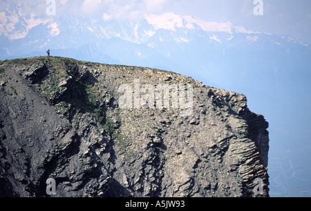 La figure solitaire qui se tenaient au-dessus d'un rocher vertical au-dessus de Crans-montana dans les Alpes Suisses en été avec des montagnes au loin Banque D'Images