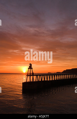 Soleil de l'été qui s'élève au-dessus de l'ancienne West Pier et de la jetée à Whitby avec Saltwick Nab visible à l'arrière-plan, Yorkshire du Nord Banque D'Images