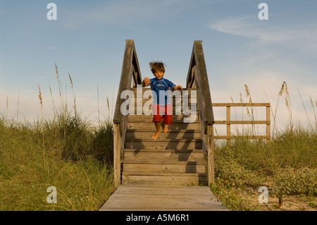 Un garçon équipé en rouge et bleu de natation fonctionne en bas les allées en direction de la plage. Banque D'Images