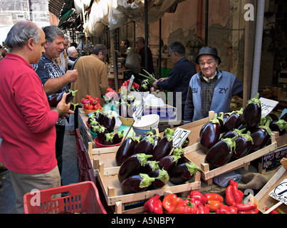 L'homme d'Aubergine : Un vieux vendeur de fruits vêtus de bleus et violets tend son affichage des aubergines correspondant Banque D'Images