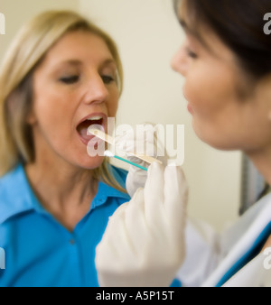 Les écouvillons médecin l'intérieur de bouche du patient pour vérifier si elle a la gorge ou le Dr strept prend un échantillon d'ADN. Banque D'Images