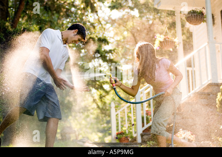 Teenage girl spraying teenage boy avec tuyau d'eau. Banque D'Images