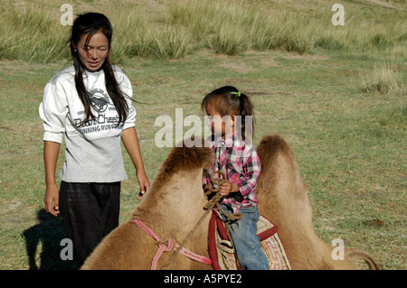 Jeune fille mongole est assis entre les deux bosses d'un chameau de Bactriane avec sa soeur regarder la Mongolie Banque D'Images