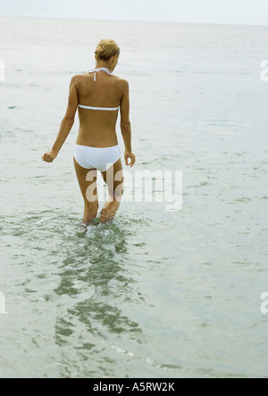 Woman in bikini, genou profondément dans l'eau, vue arrière Banque D'Images