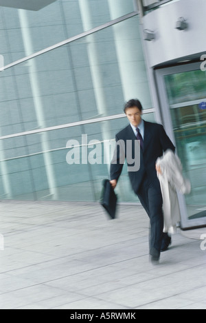 Businessman walking with briefcase et veste sur le bras, blurred motion Banque D'Images