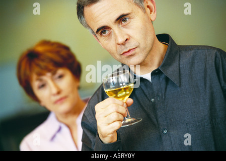 Senior man holding glass of wine, senior woman en le regardant en arrière-plan Banque D'Images