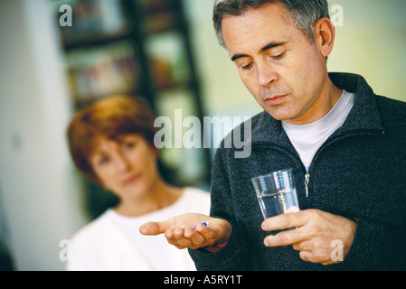 Senior man holding glass of water et comprimé, femme debout en arrière-plan Banque D'Images