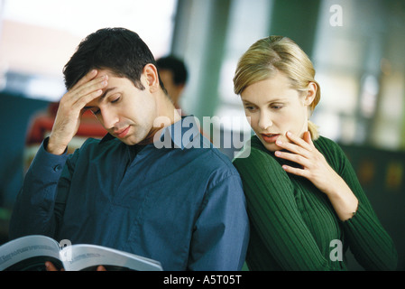 Man looking at brochure, holding head, femme regardant par-dessus son épaule Banque D'Images