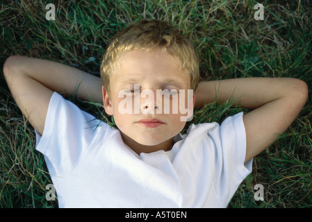 Boy lying on grass with hands behind head Banque D'Images