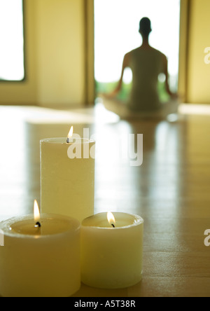 Cours de yoga, des bougies allumées alors que personne se trouve dans la position du lotus en arrière-plan flou Banque D'Images