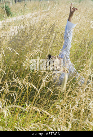 Homme assis dans les hautes herbes, pointant vers le haut Banque D'Images
