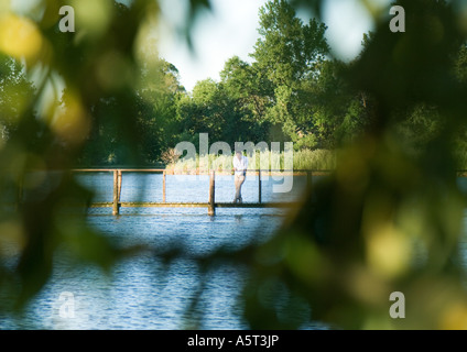 Homme debout sur la passerelle au-dessus de fleuve, dans la distance, vu à travers les feuilles en avant-plan flou Banque D'Images