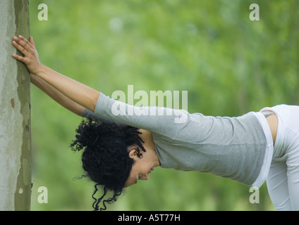 Young woman stretching contre l'arbre Banque D'Images