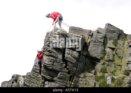 Alpinistes sur Windgather rochers sur le côté est du Peak District, Derbyshire, Angleterre. L'homme au haut des rochers est l'assurage d'un grimpeur sur le chemin vers le haut. Banque D'Images