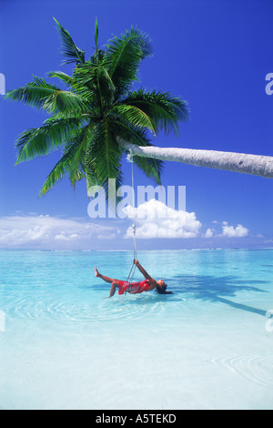 Woman laying in swing sur aqua eaux sous palmier et nuage sur Meeru Island aux Maldives Banque D'Images