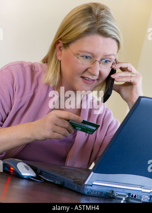 Woman shopping on line en utilisant son ordinateur portable téléphone mobile flip et une carte de crédit Banque D'Images