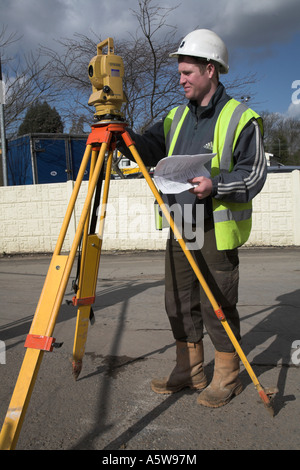 Arpenteur de jeunes hommes d'établir son théodolite, portant des vêtements de sécurité et le casque Banque D'Images