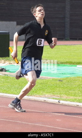Jeune homme sur une piste de course à relais en portant leurs couleurs tops compétition d'athlétisme Banque D'Images