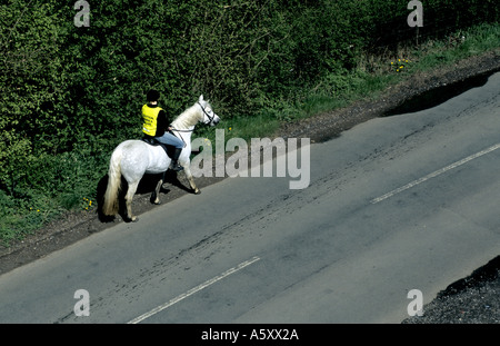 Gilet haute visibilité girl riding horse on country road, Warwickshire, England, UK Banque D'Images