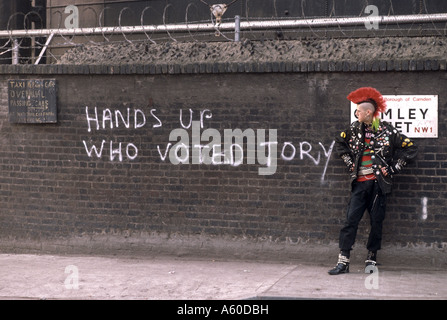 Punk debout devant mur de graffiti disant haut les mains qui ont voté Tory Banque D'Images