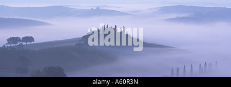 Ferme entourée de cyprès sur une colline parmi des brouillards matinaux, l'aube, Val D'Orcia, Toscane, Italie Banque D'Images