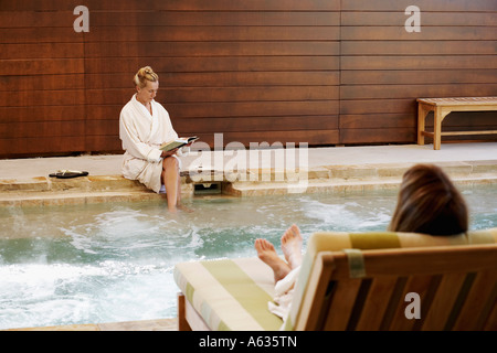 Femme couchée sur une chaise longue avec une femme mature assis sur le rebord d'un bain à remous Banque D'Images