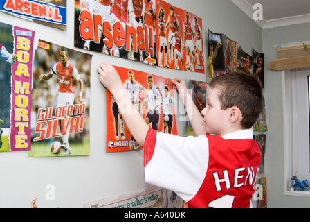 Jeune garçon supporter de football d'Arsenal en posant des affiches sur le mur de sa chambre, London, England, UK Banque D'Images